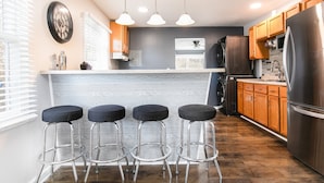 A modern kitchen with a bar area, wooden cabinets, and stainless steel appliances.