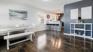 A modern kitchen with a white countertop, bar stools, and a hanging light fixture.