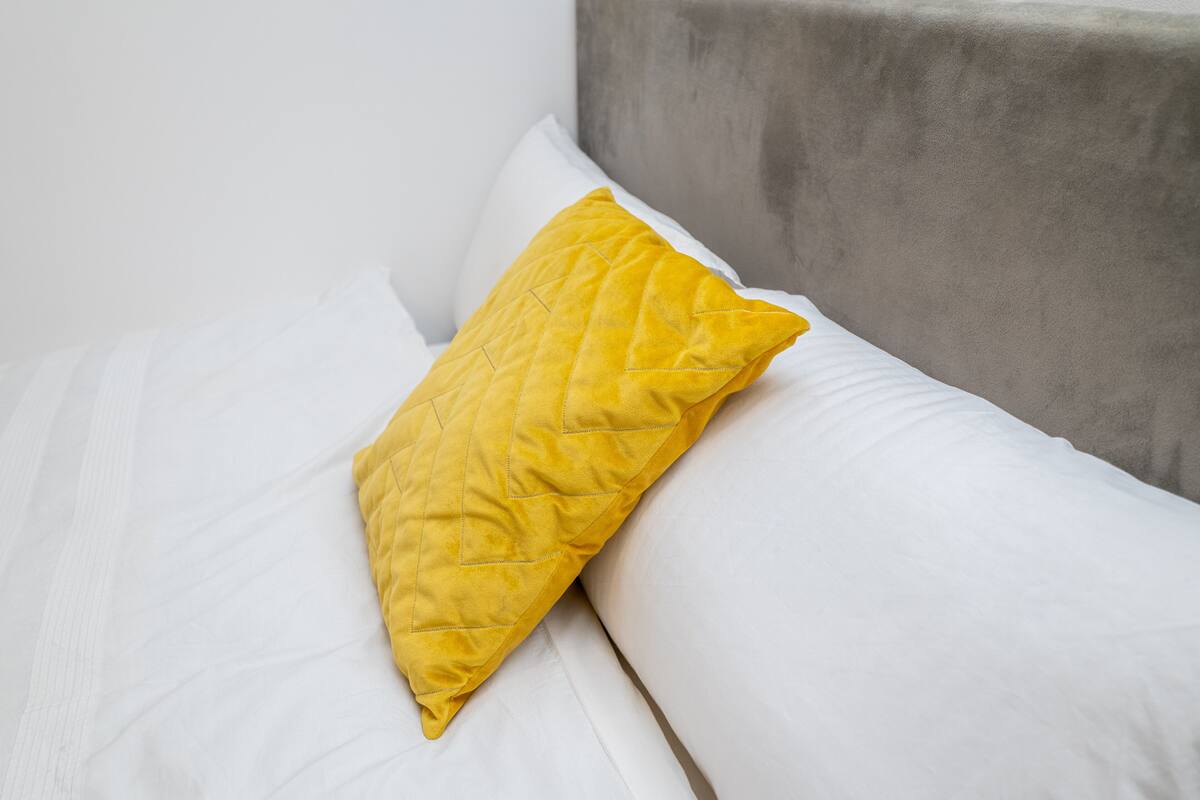 A bed with white bedding and a single yellow pillow.