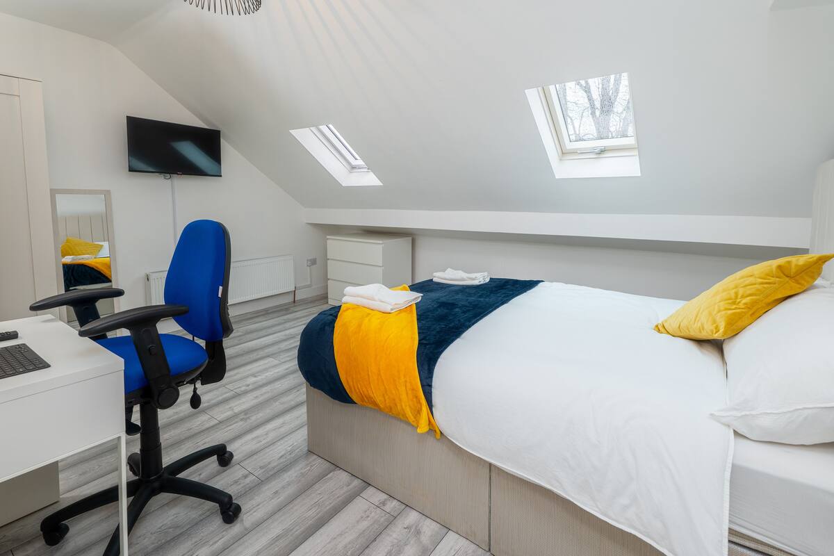 A modern bedroom with a bed, a desk, a chair, a TV, and skylights.