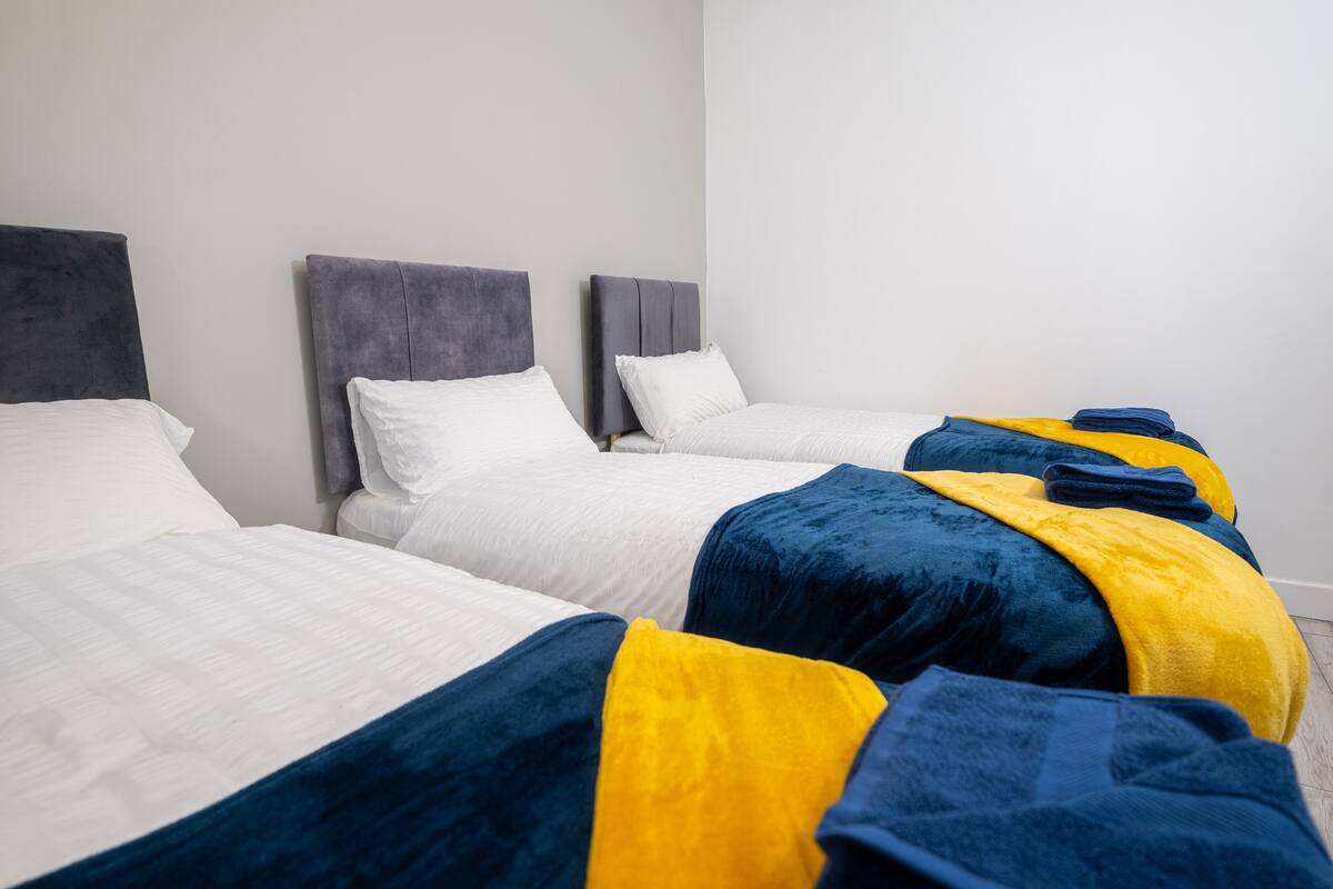 A hotel room with three beds, each with a grey headboard and white bedding.