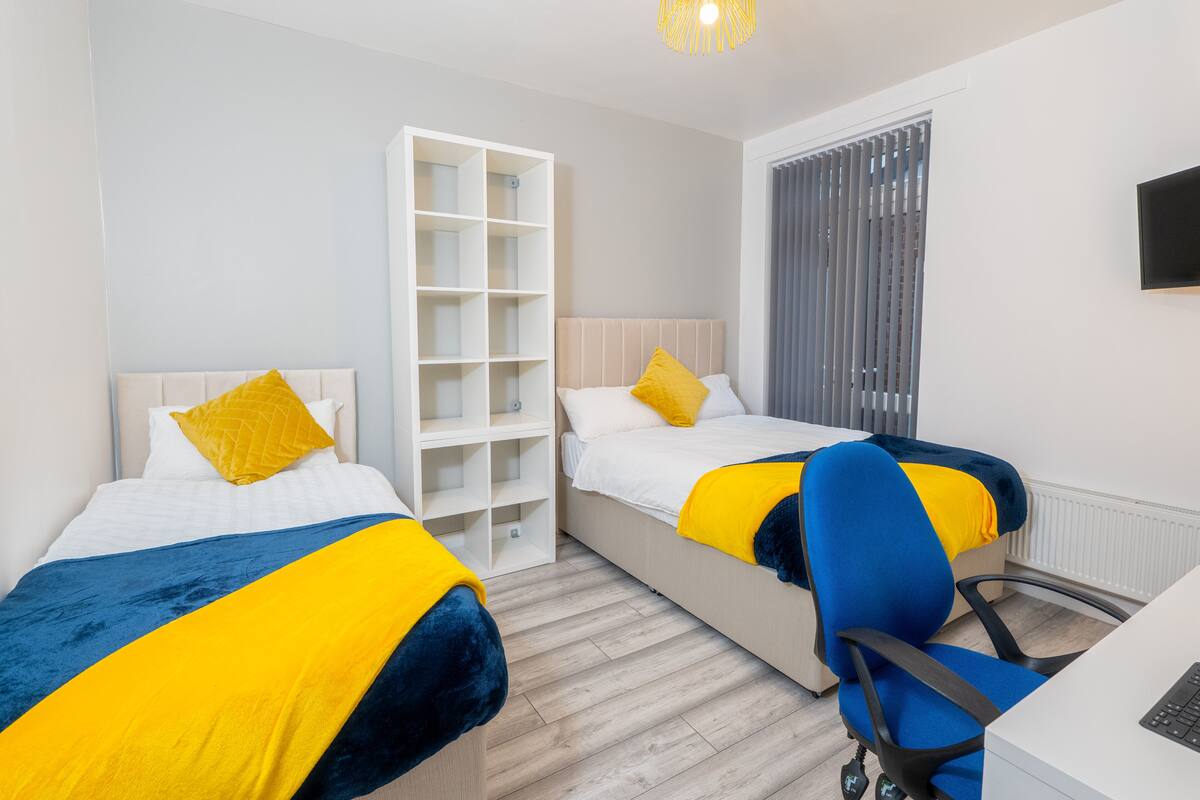 A modern hotel room with two beds, a desk, and a chair.