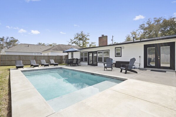 Un jardin avec une piscine, des chaises longues et un espace patio.