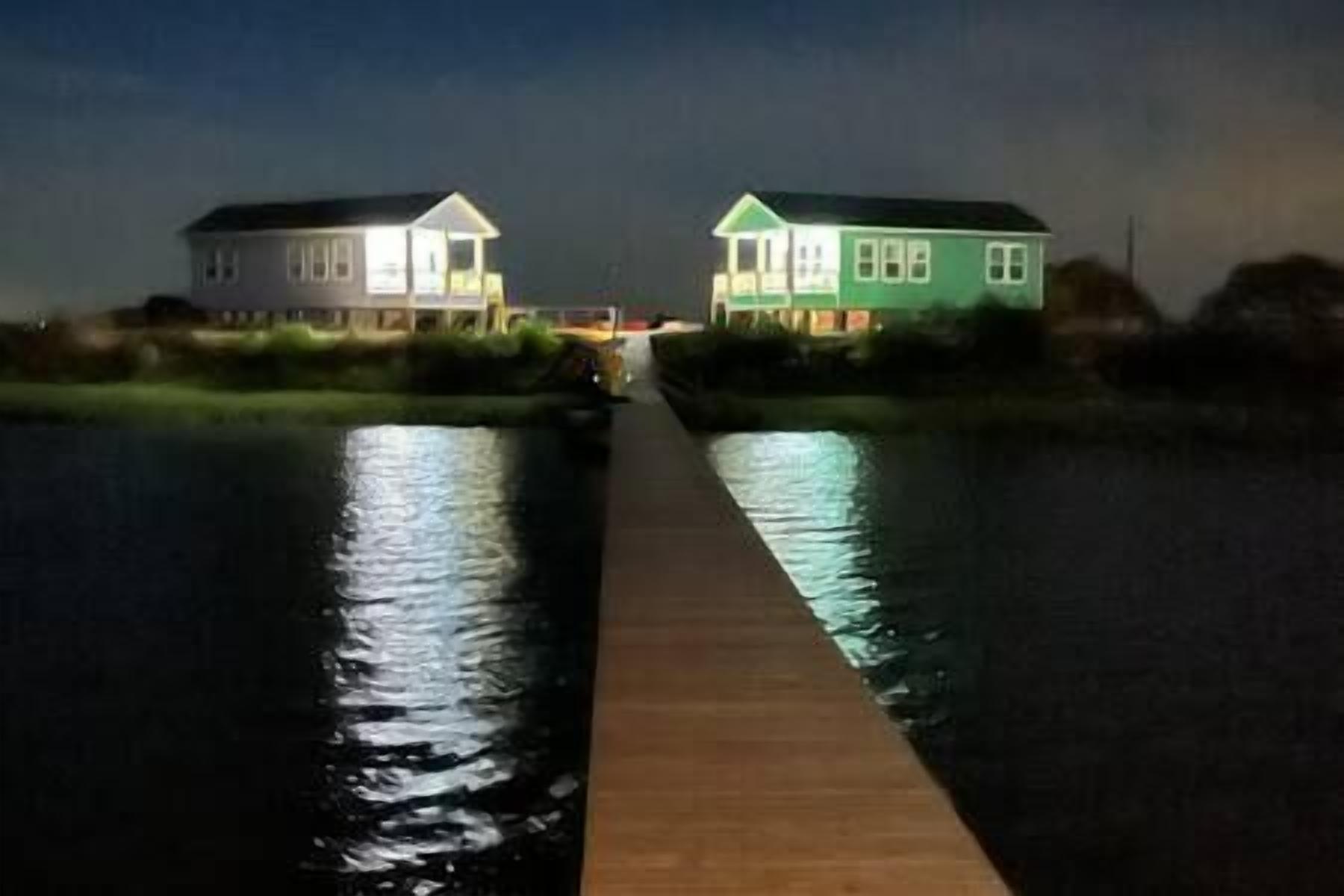 Een houten steiger die naar twee huizen aan een rustig waterlichaam leidt, 's nachts.
