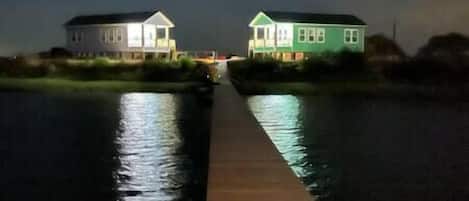 A wooden dock leading to two houses by a calm body of water at night.