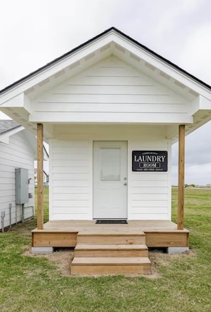 A white building with a porch and a door labeled 'Laundry Room.' - Sunset Bay Seagull Cottage (Port Lavaca)