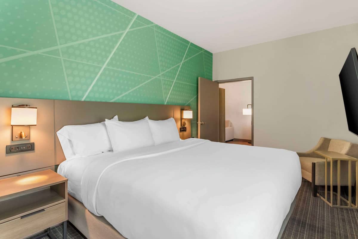 A hotel room with a large bed, bedside tables with lamps, a TV, and a seating area with a chair and a small table.