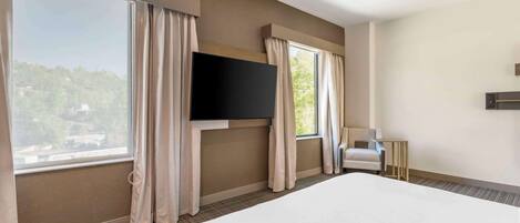 A hotel room with a large bed, a flat-screen TV mounted on the wall, and a window with curtains.