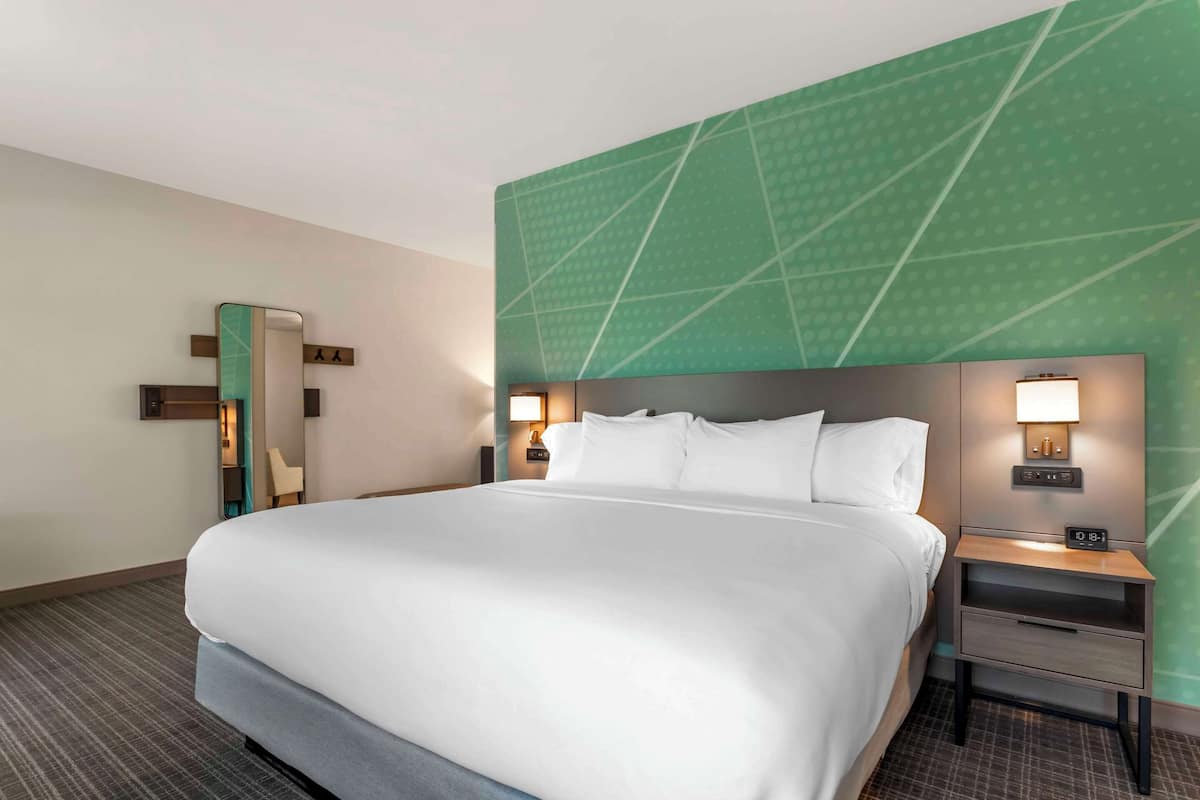A hotel room with a large bed, a nightstand with a lamp, a mirror, and a green accent wall.