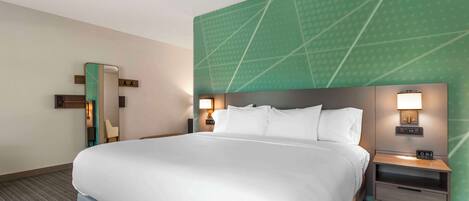A hotel room with a large bed, a nightstand with a lamp, a mirror, and a green accent wall.