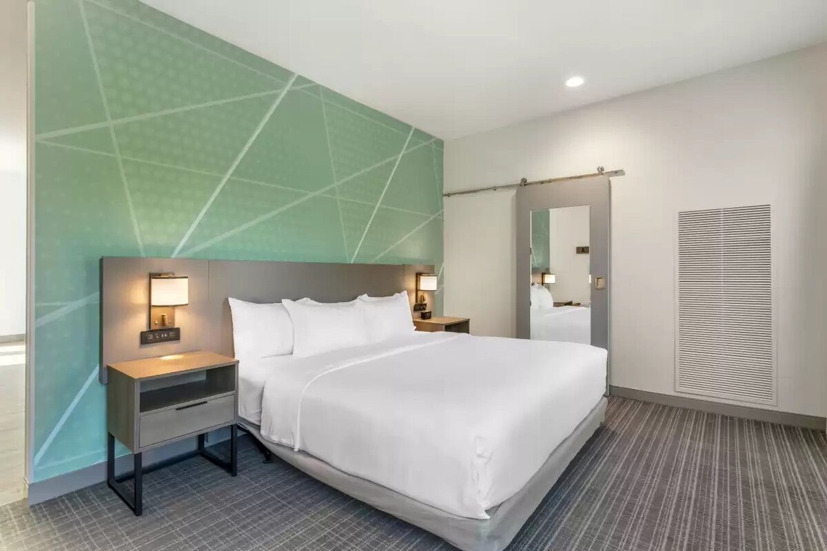 A hotel room with a large bed, two bedside tables with lamps, a mirror, and a wall-mounted heater.