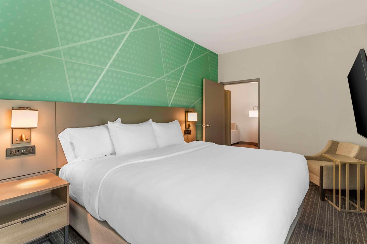 A hotel room with a large bed, bedside tables, a TV, and a seating area.