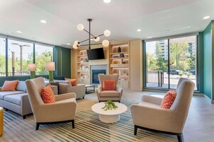 Una sala de estar moderna con sofás, una mesa de centro y un televisor. Amplias ventanas ofrecen vistas al exterior.