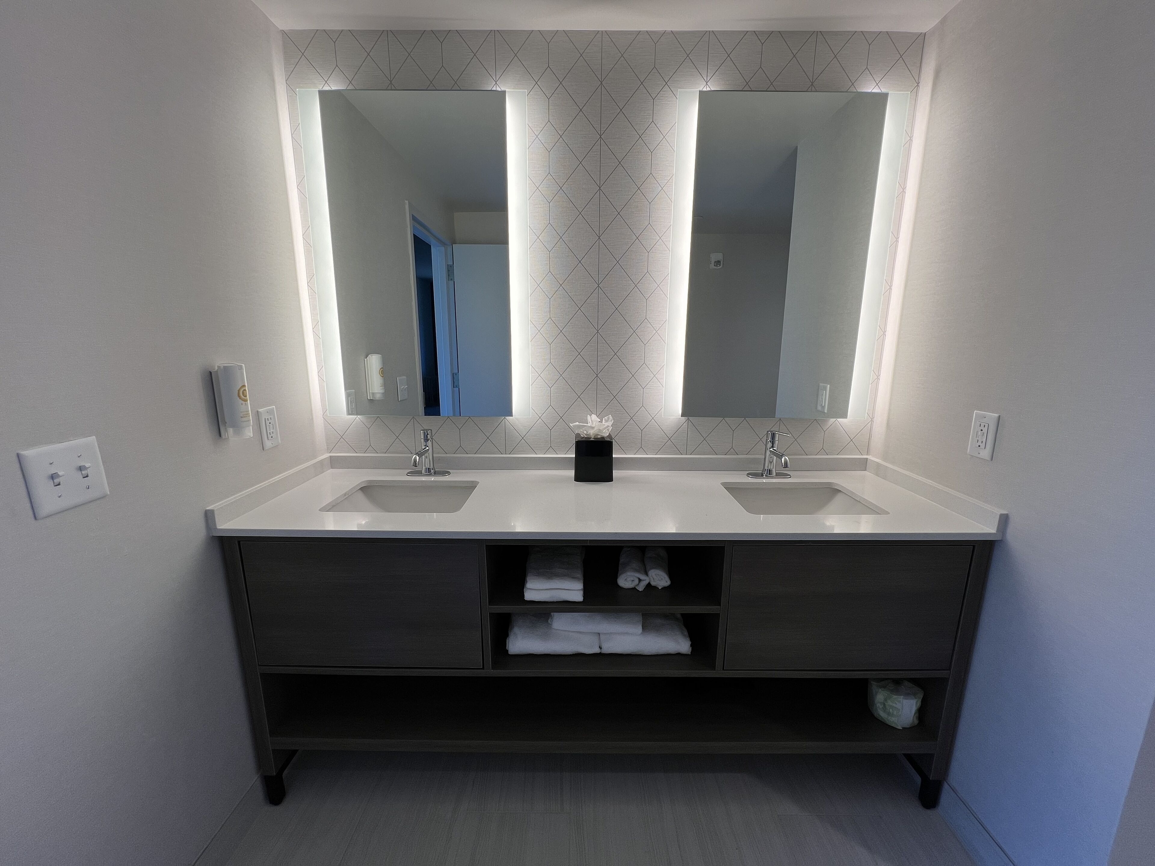 A modern bathroom with two sinks, a large mirror, and a dark vanity with storage drawers.