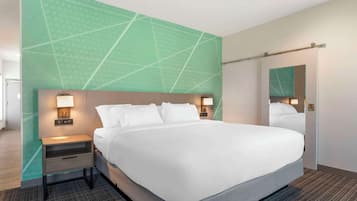 Quarto de hotel moderno com uma cama grande, uma mesa de cabeceira com abajur e um espelho na parede.