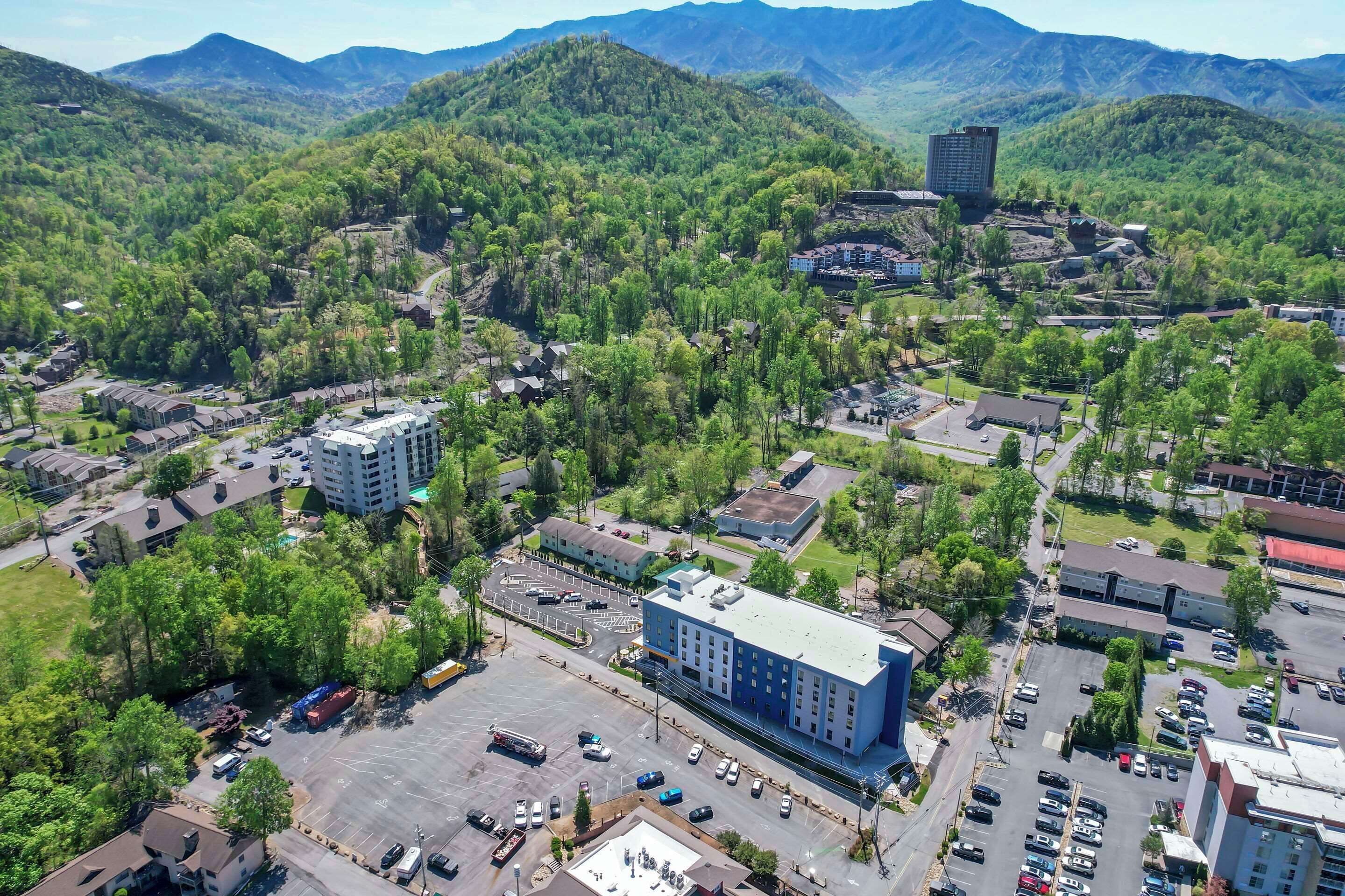 Vue aérienne d’une ville avec un grand bâtiment doté d’un toit bleu, entouré de verdure et de montagnes.