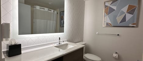 A modern bathroom with a large mirror, white sink, and a toilet. There is a towel rack and a towel shelf.