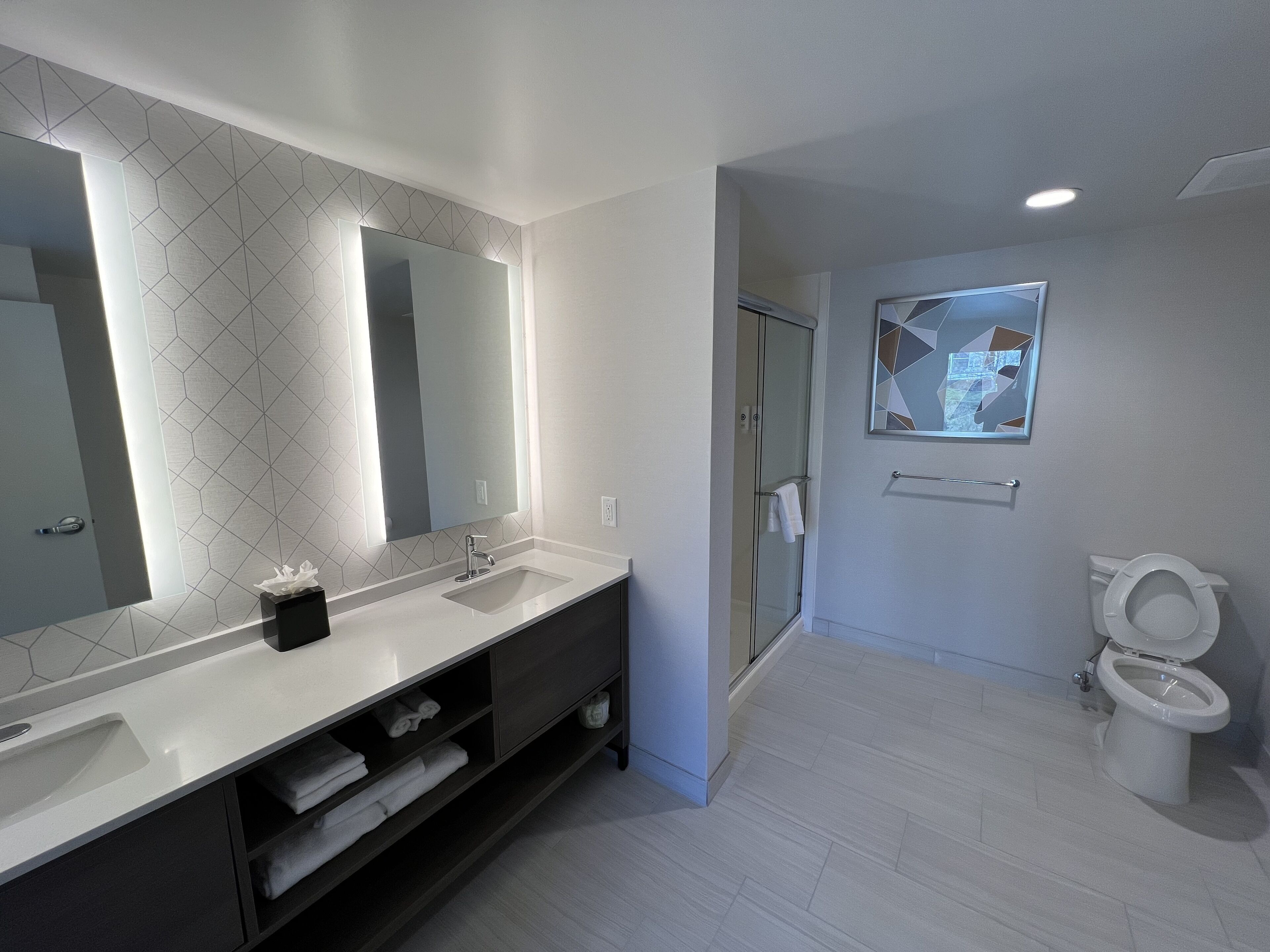 A modern bathroom with a large mirror, a sink, a toilet, and a shower area.