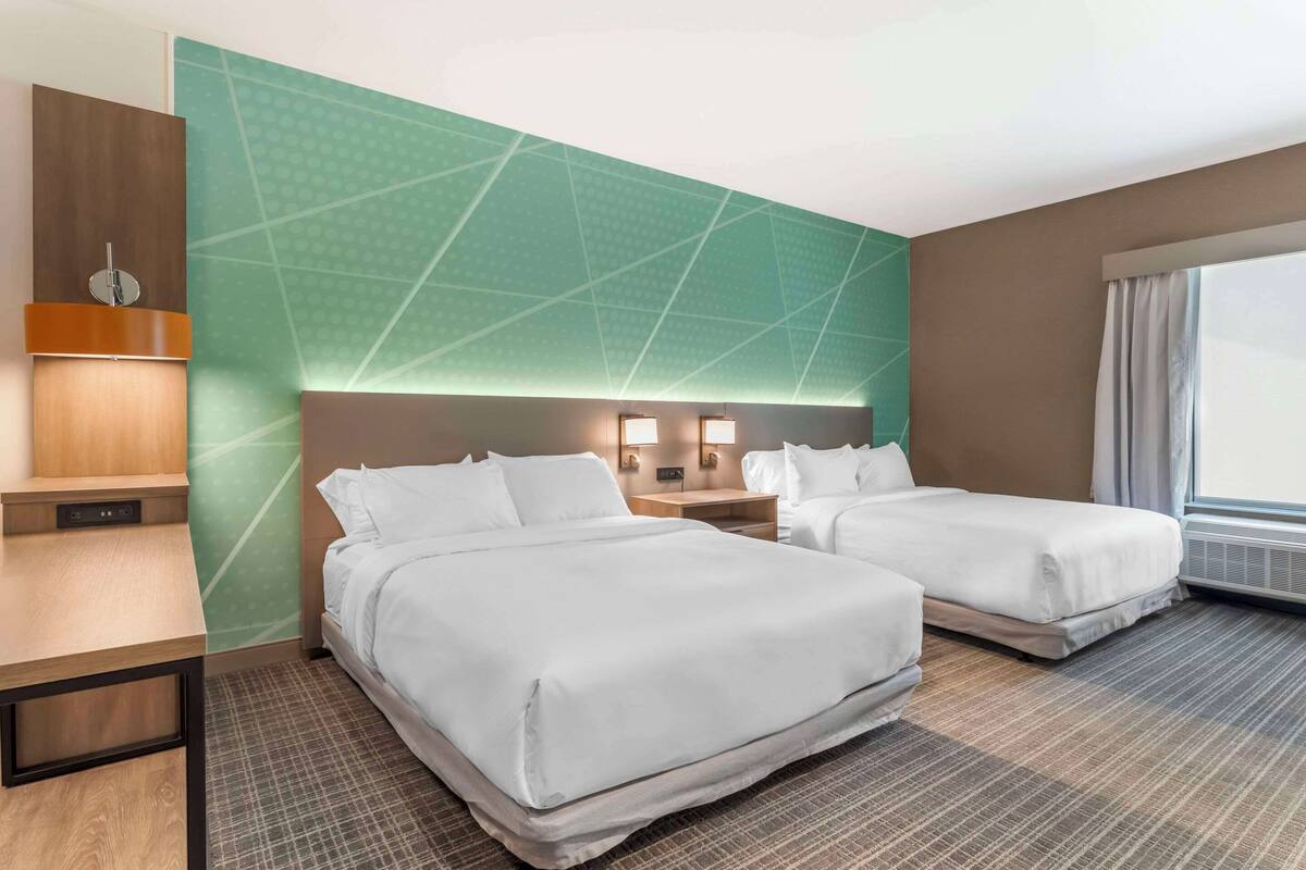 A hotel room with two beds, a desk, a nightstand, and a large window.