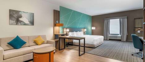A hotel room with a bed, a sofa, a small table, a desk, and a chair.