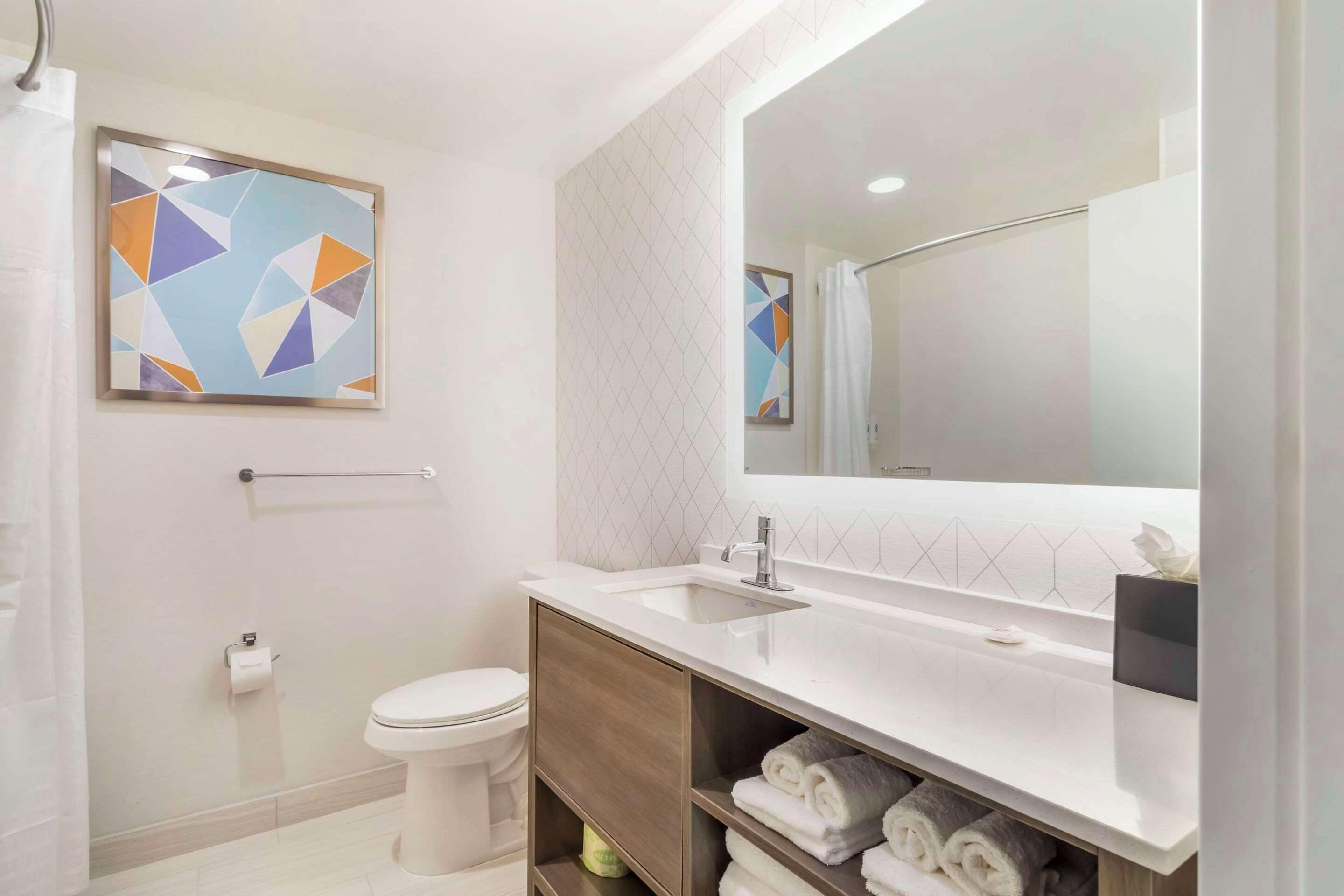 Une salle de bain moderne équipée de toilettes, d’un lavabo et d’une douche. On y trouve un porte-serviettes et un miroir au-dessus du lavabo.