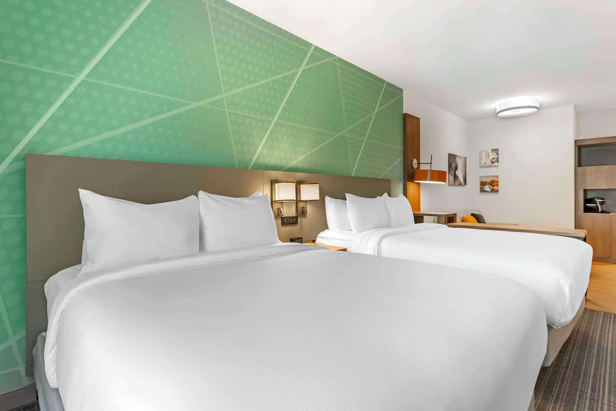 A hotel room with two beds, a green patterned wall, and a small kitchenette.