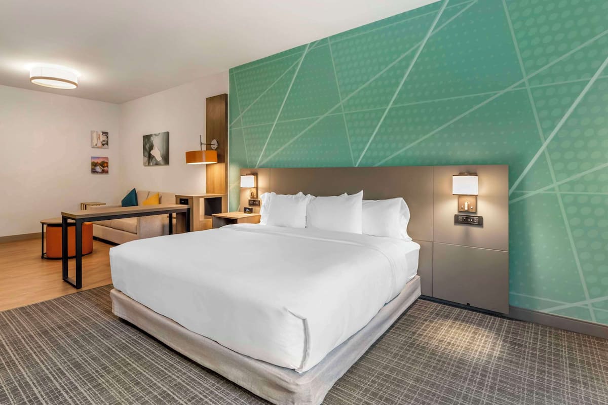 A hotel room with a large bed, bedside tables, a desk, and a green accent wall.