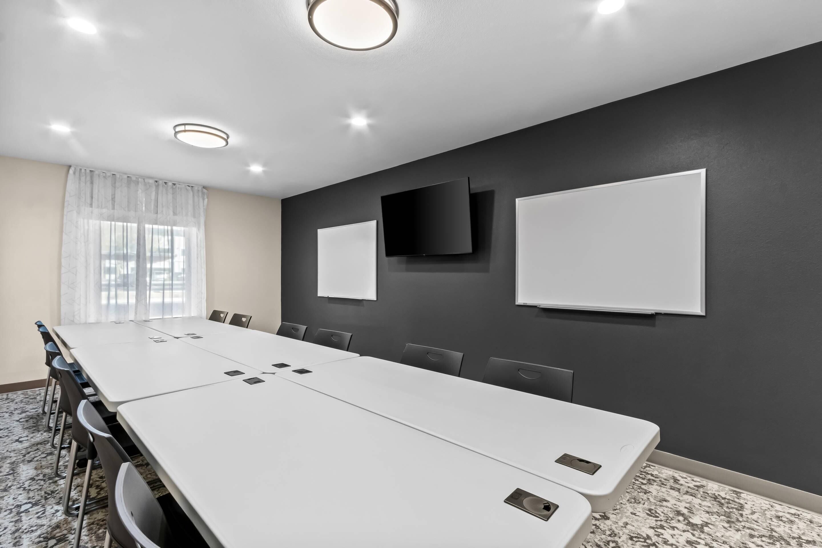 A conference room with a long table, chairs, a whiteboard, a TV, and a window with curtains.