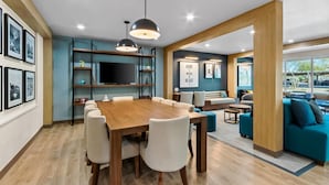 Una sala moderna con una mesa de comedor de madera, sillas blancas, un sofá azul y un televisor en un estante.