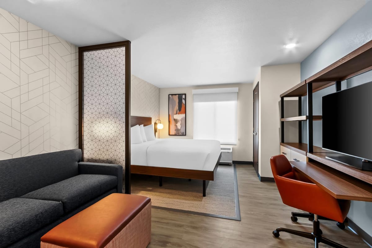 Una habitación de hotel con cama, escritorio con televisor, sofá y una mesita.