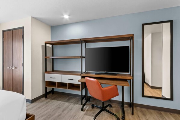 A room with a desk, chair, wardrobe, and a large mirror.