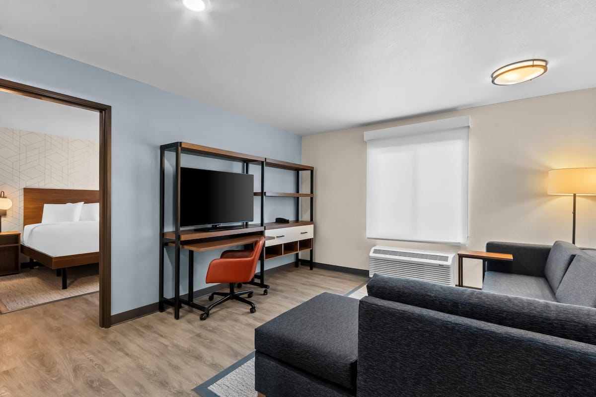 Una habitación de hotel con una cama, un escritorio con computadora, televisor, sofá y lámpara.