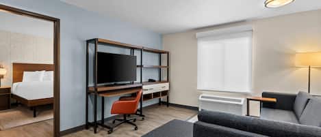 A hotel room with a bed, a desk with a computer, a TV, a sofa, and a lamp.