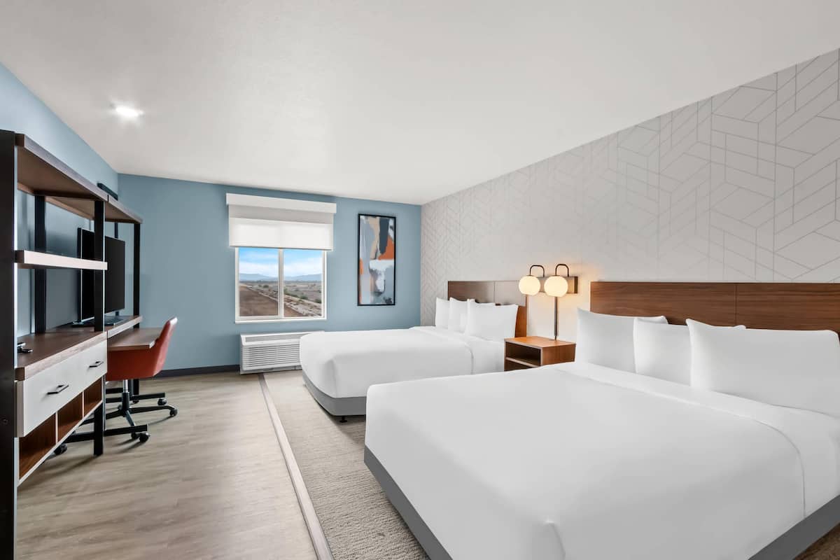 Habitación de hotel con dos camas, un escritorio con silla, un televisor y una ventana con vistas.
