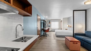 Una habitación de hotel moderna con kitchenette, una cama, un sofá y una pequeña mesa.