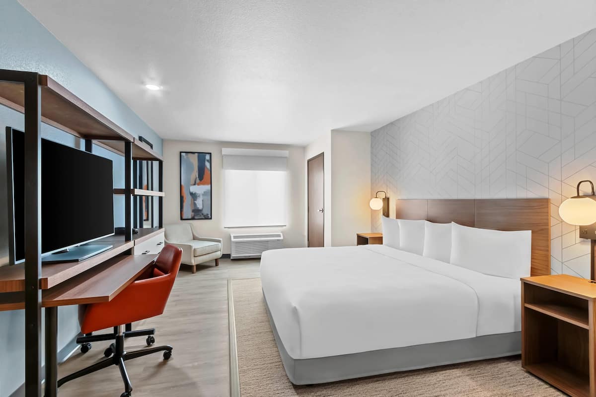 Una habitación de hotel moderna con una cama grande, un escritorio con una computadora, una silla y un televisor.