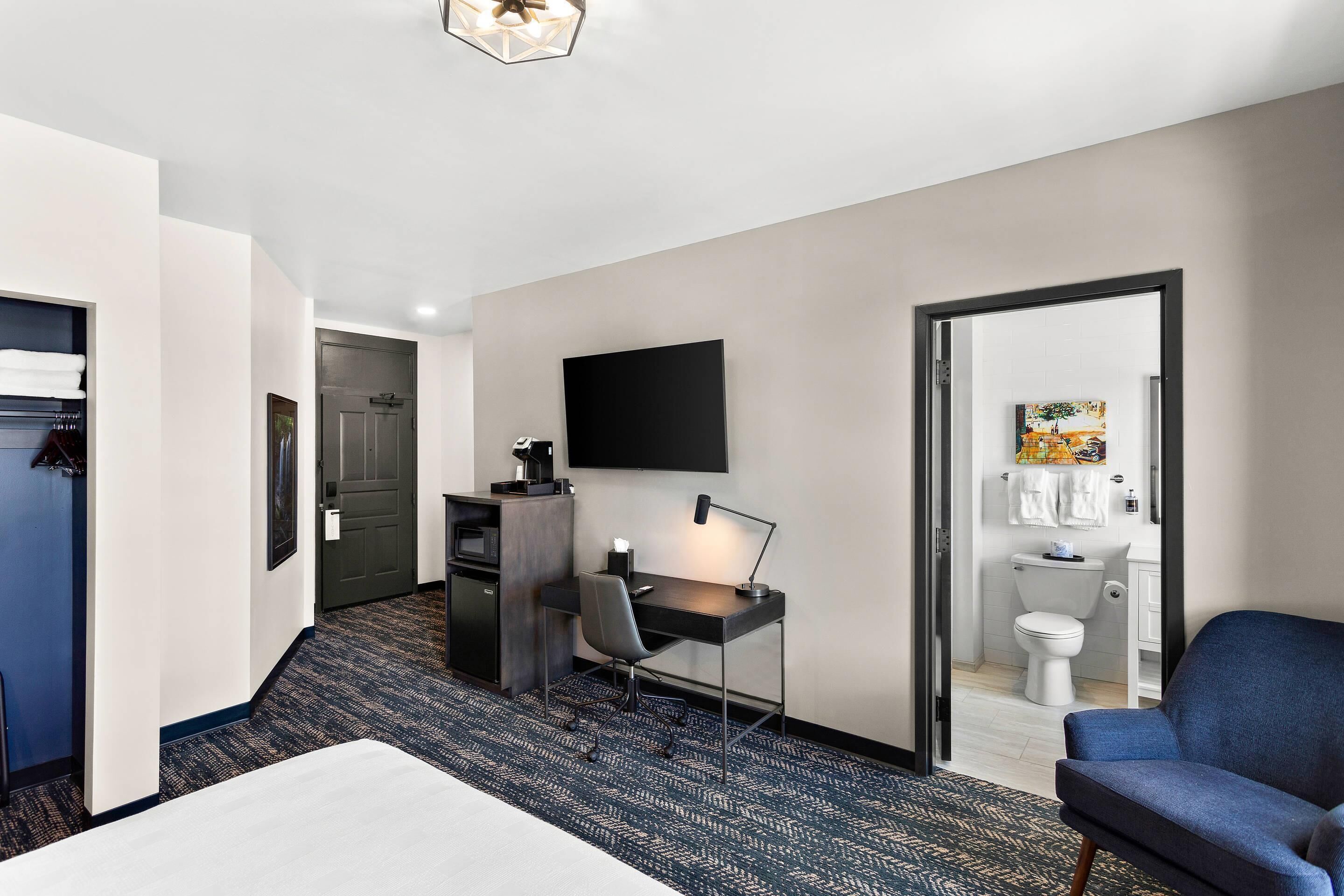 Una habitación de hotel con escritorio, silla, cama y televisor montado en la pared.