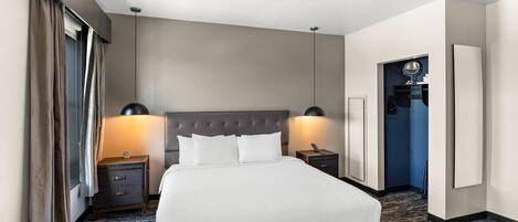 A hotel room with a large bed, two bedside tables with lamps, a wardrobe, and a bathroom visible through an open door.