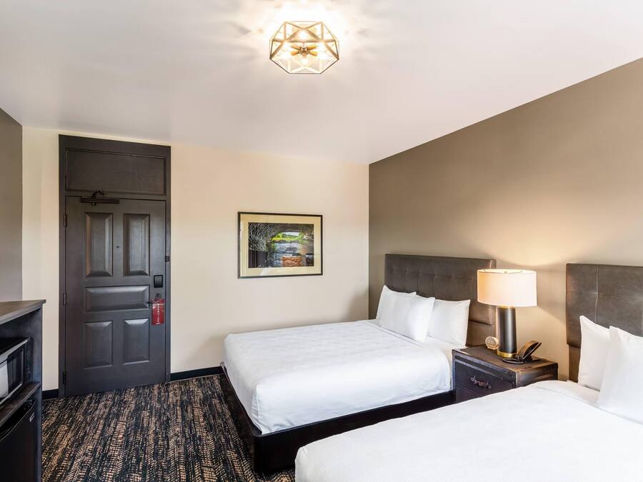 A hotel room with two beds, a desk, a chair, a door, and a ceiling light fixture.