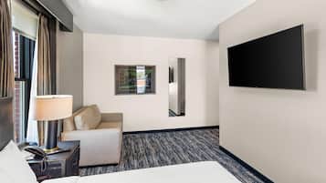 Habitación de hotel con cama, escritorio con lámpara, televisor montado en la pared y vistas al exterior a través de una ventana.
