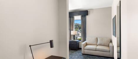 Une chambre d’hôtel équipée d’un bureau, d’une lampe, d’un canapé, d’une fenêtre avec des rideaux et d’un tapis à motifs.