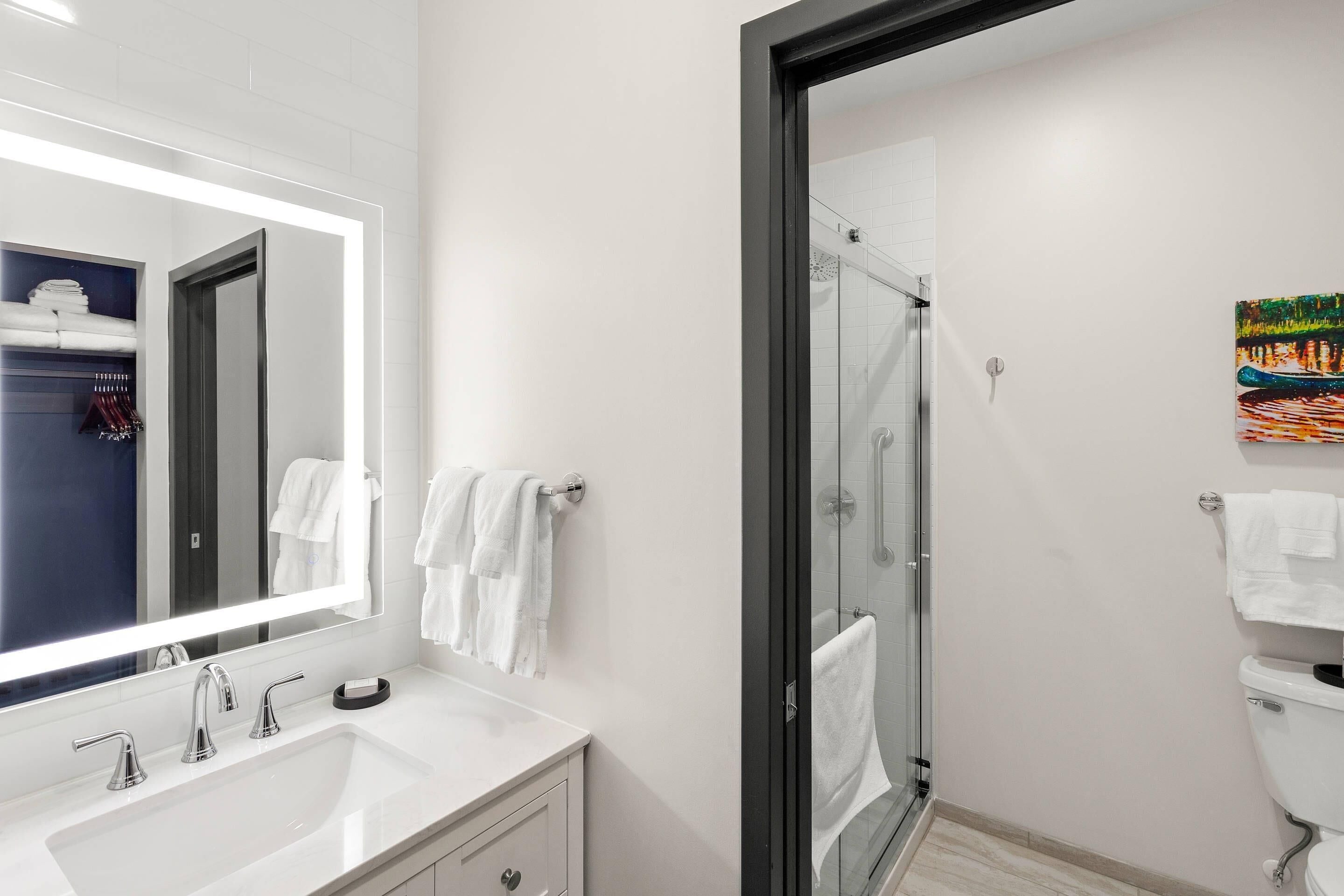 A modern bathroom with a large mirror, white sink, and a glass-enclosed shower.