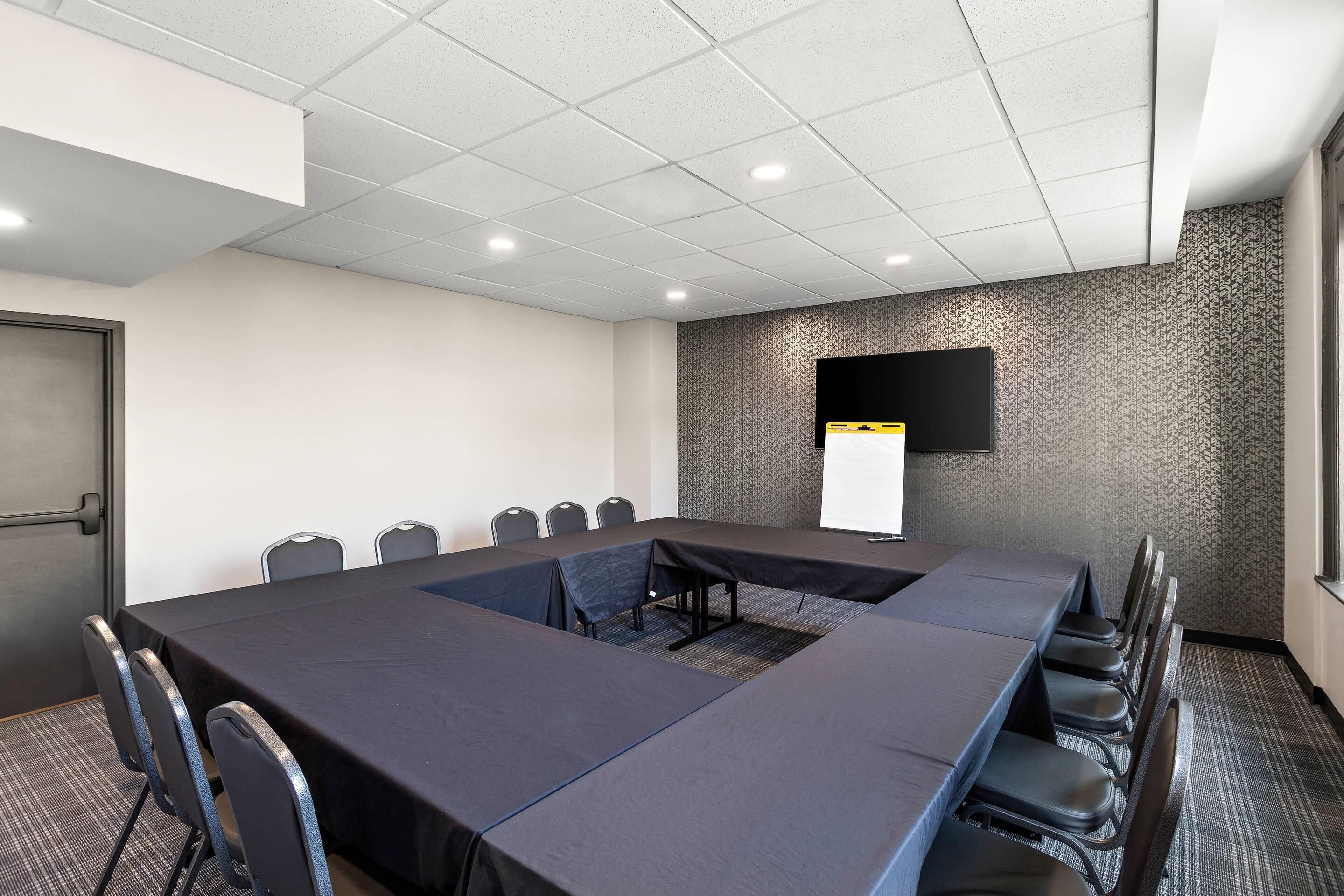 Un salón de conferencias con una larga mesa, sillas, una pantalla de proyector y un muro con diseño.