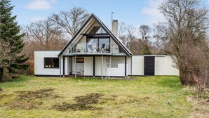 Ett modernt hus med ett triangulärt tak, en balkong med utomhusmöbler och en skorsten.
