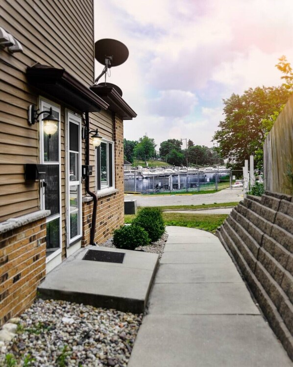 A building with a satellite dish, a brick exterior, and a pathway leading to a marina with boats. - Beach Lake Michigan King Bed Pet Friendly (Kenosha)