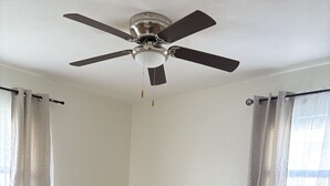 Un dormitorio con cama, mesitas de noche, ventilador de techo y cortinas.