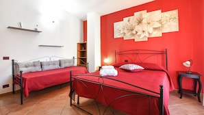 Una camera da letto con due letti, un muro rosso e un grande quadro con motivi floreali.