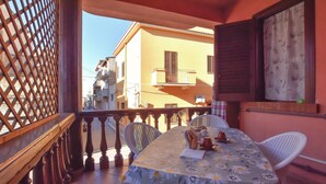 Un balcone con tavolo e sedie, affacciato su una strada con edifici.