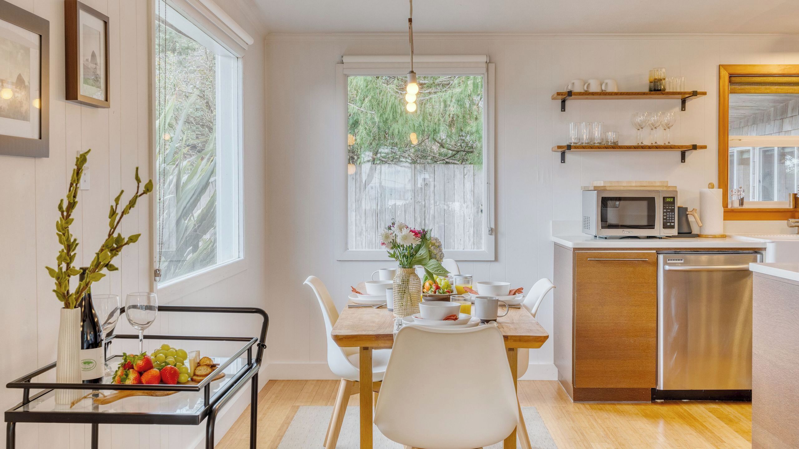 A modern kitchen with white cabinets, a wooden dining table, and a built-in microwave.