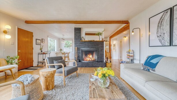 A modern living room with a fireplace, wooden beams, a sofa, and a dining area. - Four Bears by Avantstay Walk to Beach, Hot Tub, Ocean View (Arch Cape)
